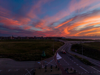 Aerial sunset view of coastal town winding road with lone vehicle leads past grassy field and...