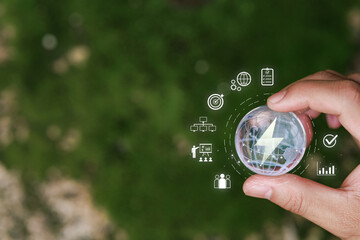 Hand Holding Clear Globe with Lightning Symbol Surrounded by Digital Icons Representing Renewable Energy and Sustainable Development Concepts