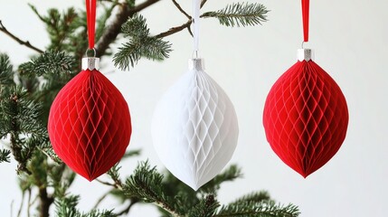 Three decorative honeycomb ornaments in red and white hanging from a Christmas tree branch.