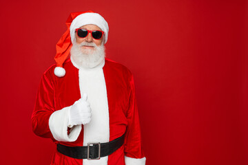 Close up portrait of funny happy old bearded Santa Claus face wearing hat, glasses, looking at camera, laughing, standing on Merry Christmas, Happy New Year isolated on red background, copy space