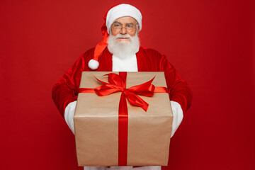 Happy funny old bearded Santa Claus wears costume holds present, Merry Christmas giftboxes wrapped with red ribbon, laughing giving gift box having fun isolated on red xmas background.
