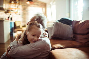Child granddaughter hugging senior grandparent contentedly on living room sofa