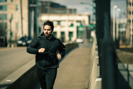 Young adult man running with determined focus on city bridge