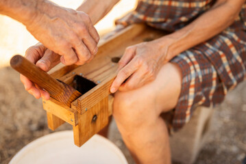 Man placing olive into wooden cracking machine during traditional preparation
