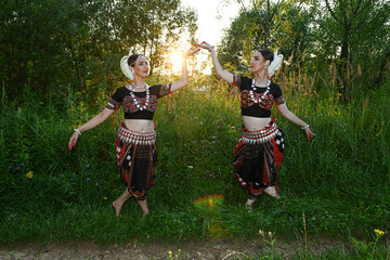 Indian women dancers in beautiful costumes on a green background of nature in a park with the rays of the sun at sunset in dance poses