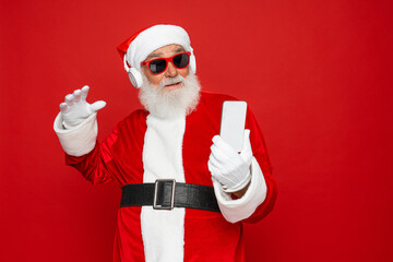 Stylish trendy grandfather aged mature Santa tradition winter costume headwear spectacles white beard take christmastime selfie picture have video zoom call waving hand isolated red background