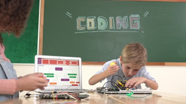 Caucasian smart boy fixing main board by using screwdriver at stem technology lesson while smiling student working together to inspect electronic machine at table with laptop display code. Pedagogy.