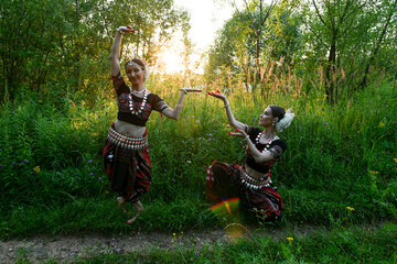 Indian women dancers in beautiful costumes on a green background of nature in a park with the rays of the sun at sunset in dance poses