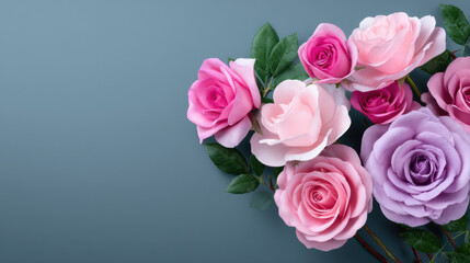 A beautiful floral arrangement featu light pink, hot pink, and lavender roses with green leaves is displayed on a soft blue background providing copy space.
