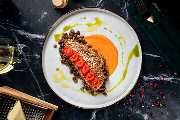 Flavorful lentil dish served with sliced tomatoes, cheese and creamy sauce on a modern plate
