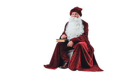 A man dressed in a red robe and hat with a white beard sits holding a book on a plain white surface no background