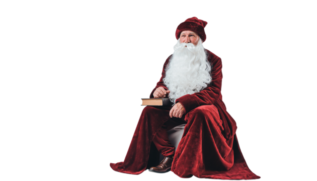 A man dressed in a red robe and hat with a white beard sits holding a book on a plain white surface no background - Powered by Adobe