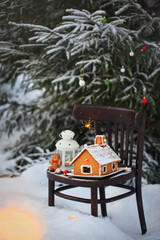 Gingerbread house and holiday decoration on chair in snow winter outdoor background