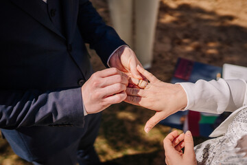 Groom placing wedding ring on bride's finger during outdoor ceremony, capturing the intimate moment of love and commitment in a beautiful natural setting