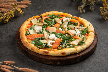 Fresh pizza topped with smoked salmon, arugula, cheese, and cream served on dark textured background