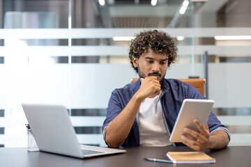 Business portrait of a young Indian man working seriously and thoughtfully in the office using a tablet