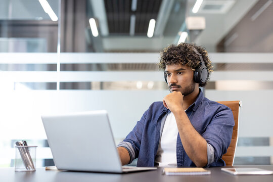 Serious and focused young Indian man in headphones working in the office on a laptop