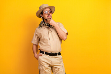 Man in safari style outfit with hat scarf and sunglass stands against bright yellow background...