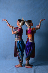Fototapeta premium Indian female dancers in beautiful costumes on a blue background in the studio in dance poses