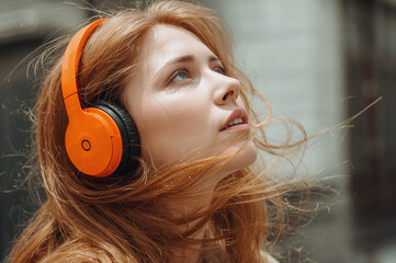 Close-up profile portrait of a young red-haired woman wearing bright headphones, sunlight, shallow depth of field