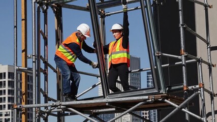 scaffold teamwork at urban construction site two workers in helmets and high visibility vests inspect metal - Powered by Adobe