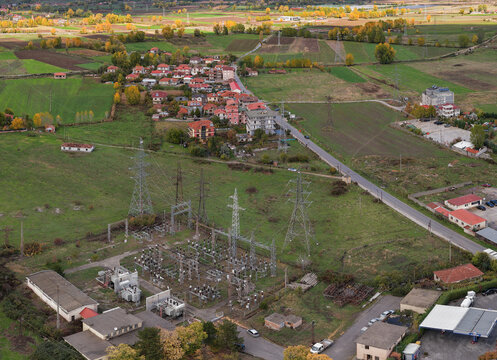 Autumn aerial view of Korçë’s outskirts with open fields, a village and an electrical substation surrounded by seasonal colours.