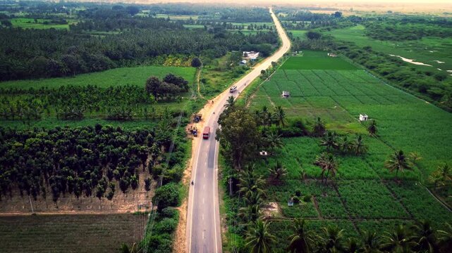 Aerial view of a National highway passing through lush green farmland and village landscapes in South India.