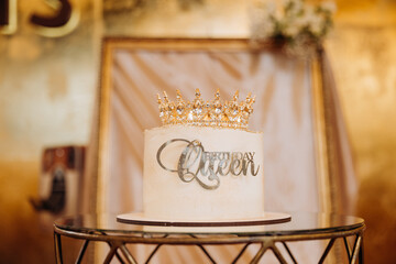White birthday cake with golden crown and Birthday Queen topper on elegant party table