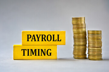 PAYROLL TIMING - words on yellow wooden blocks on the background of stacks of coins