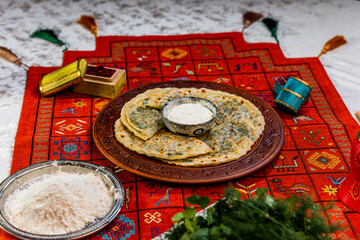 Close-up of traditional Azerbaijani herb qutab served on a rustic plate. Thin crispy flatbread filled with fresh mixed herbs, folded and lightly toasted, presented with yogurt sauce and authentic nati