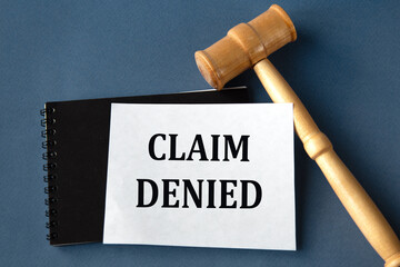 CLAIM DENIED - words on a white sheet on a black notebook with a judge's gavel in the background