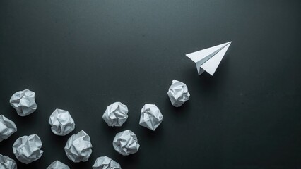 A paper airplane leading a group of crumpled paper balls on a dark surface.