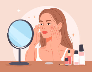 Young woman applying facial cream in front of a mirror, with cosmetic products displayed on a table, showcasing a skincare routine.