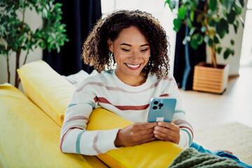 Casual home moment a young woman on yellow couch using smartphone in bright living room