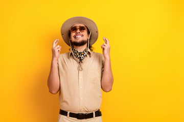 Smiling man in safari outfit with hat scarf and sunglass stands against yellow background evoking adventure travel and summer exploration
