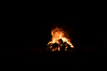 A large bonfire burning brightly in the dark night with flames reaching high into the air above it