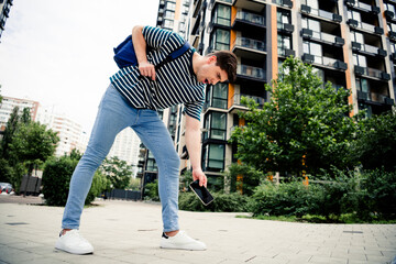 Young man reaching for dropped smartphone on a sunny urban street surrounded by modern residential buildings