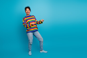 Joyful young woman dancing in a rainbow striped sweater against a blue background