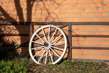 Obraz premium White wagon wheel leaning on rustic brick wall