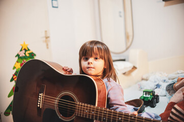 A little girl is learning to play an acoustic guitar 