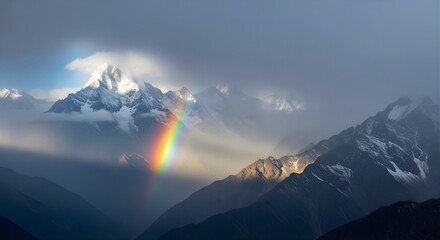 A vibrant rainbow arches across a cloudy mountain landscape with snow capped peaks and dramatic lighting