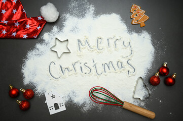 Top view of Christmas baking background with flour text, gingerbread shapes, rolling pin and red baubles. Great for greeting cards, culinary ads and festive visual design.