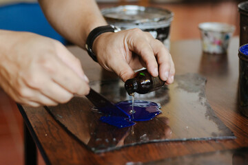 Hands diluting blue oil lithographic printing ink with oil on a glass slab, preparing for printing process