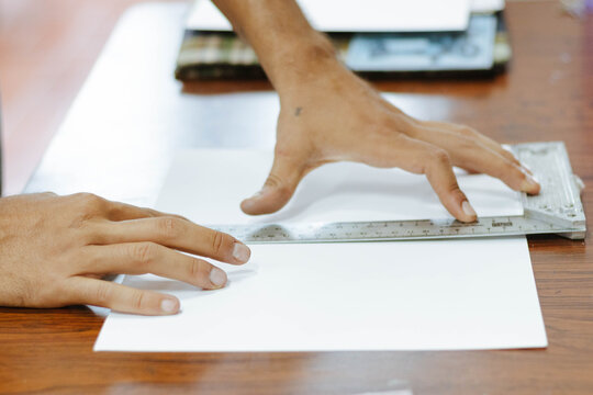 Art student using a ruler on paper, drawing lines for architecture and design project in a classroom