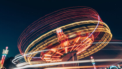 Amusement ride with light trails at night under starry sky.
