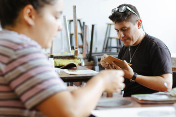 Man focusing on an object while learning new crafting techniques during an art workshop, engaging in creative work