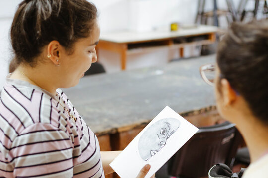 Young woman showing art drawing to friend, learning artistic skills in creative workshop, sharing ideas