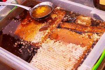 Texture of honeycombs close up. Yellow wax honeycombs with honey in plastic containers. Sale of homemade honey at the fair