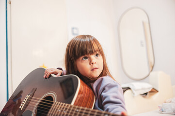 A little girl is learning to play an acoustic guitar 
