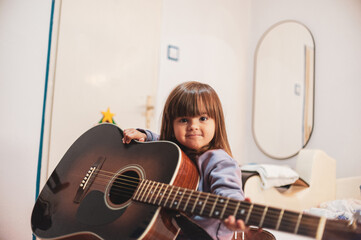 A little girl is learning to play an acoustic guitar 